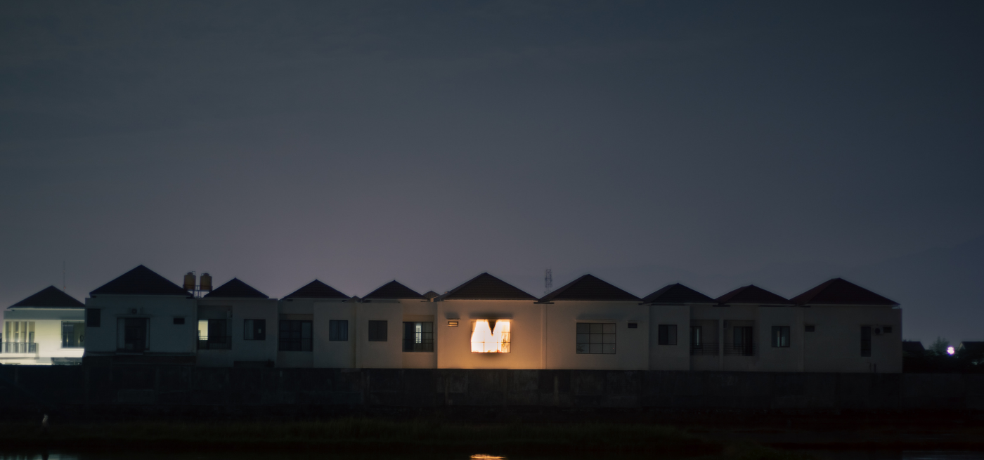 Fila de casas ao anoitecer, com uma janela iluminada a destacar-se